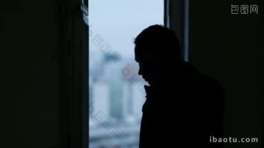 男人在窗户附近打电话，黑色的剪影在模糊的城市背景在窗口